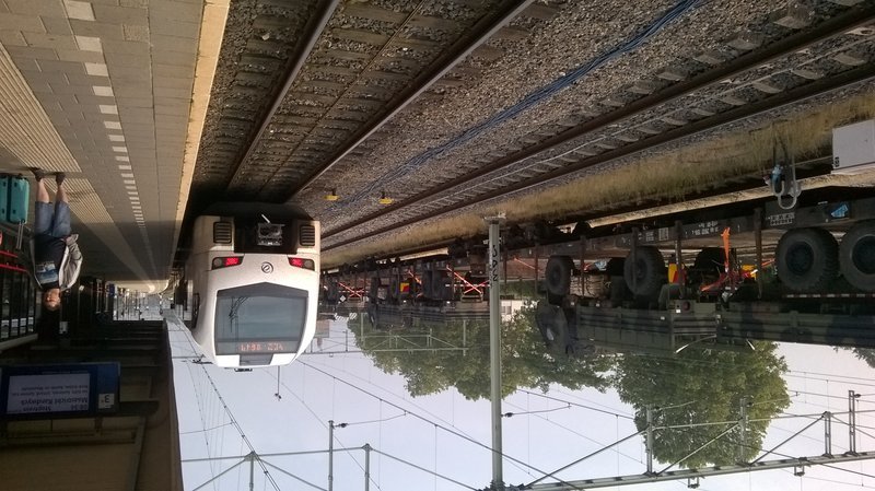 Arriva FLIRT op het station. Links passeert een goederentrein met legervoertuigen het station